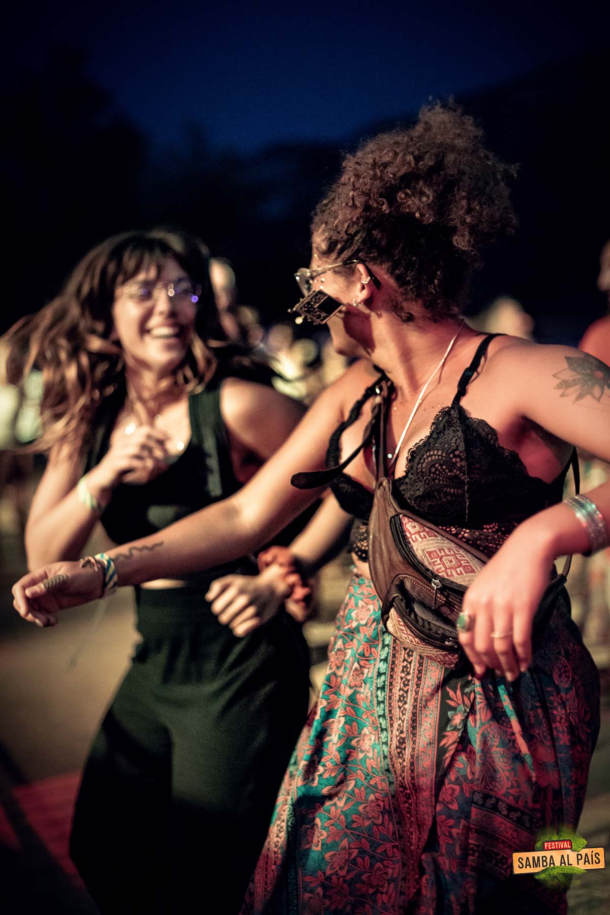 Deux jeunes femmes joyeuses qui se regardent et dansent devant un concert de Samba al País